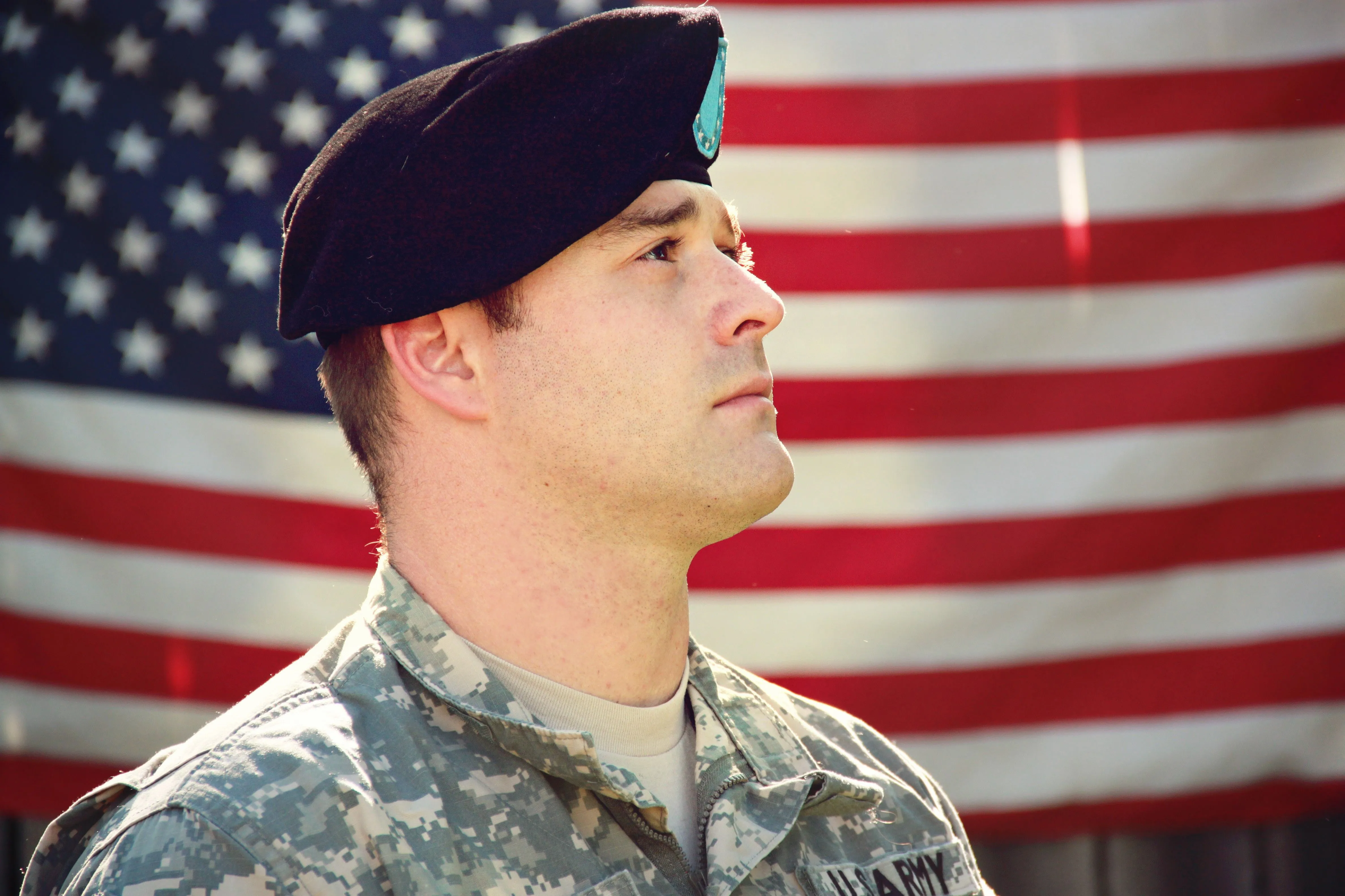 U.S. Army service member standing in front of an American flag during military service.